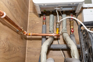 Natural gas valves and copper pipes in a modern home boiler room with ceramic tiles.
