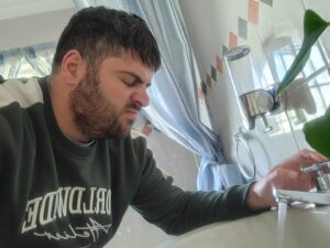 Homeowner reacting to an unpleasant smell coming from a bathroom basin drain, a common warning sign of a developing drain blockage.