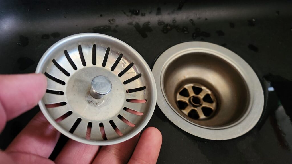 Kitchen sink strainer removed for cleaning to prevent food debris from causing blocked drains and unpleasant drain smells.