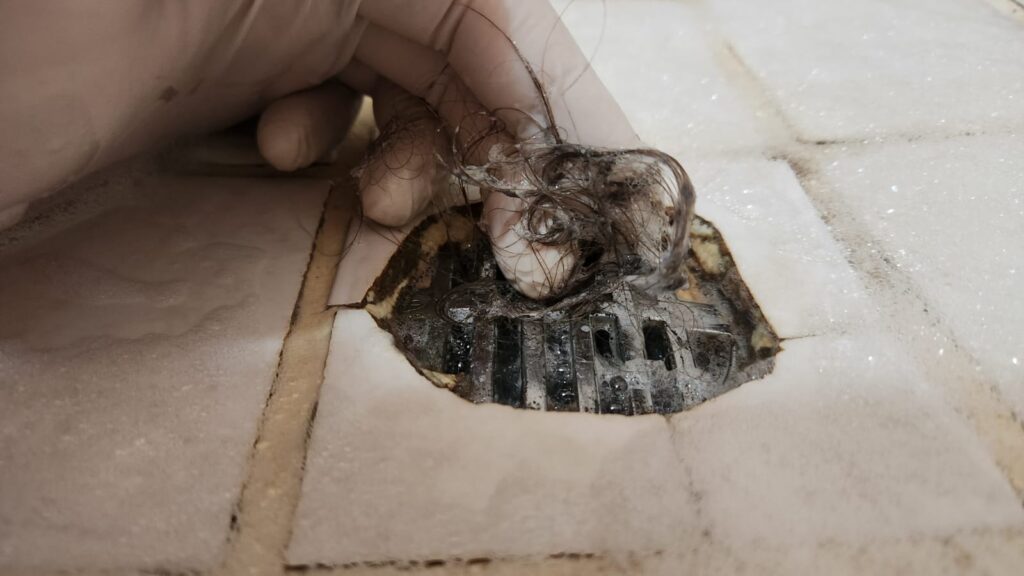 Hair being removed from a blocked shower drain during a homeowner maintenance check to improve water flow and prevent drain blockages.