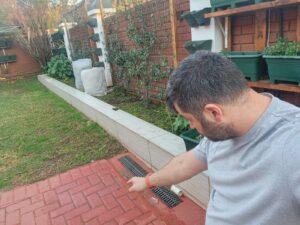 Homeowner pointing to a damp patch on outdoor paving that may indicate a hidden underground water leak.