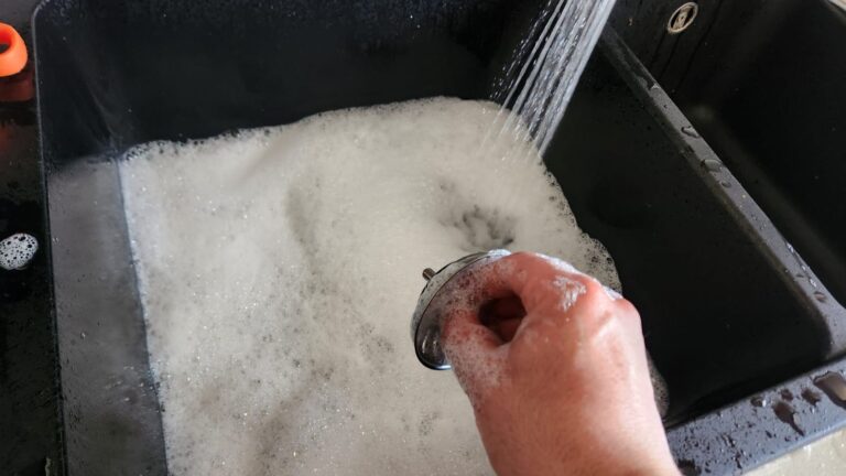Kitchen sink filling with water due to a blocked drain while the sink strainer is being removed to inspect the blockage.