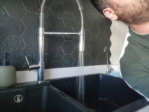 A homeowner running water into a kitchen sink to check whether the drain is flowing freely after cleaning and maintenance.